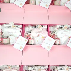 A glimpse of a bulk order for a bride tribe, all packed and ready to go. Each pink box is filled with personalized goodies like custom "Bridesmaid Times" newspapers, eye masks, and monogrammed necklaces.