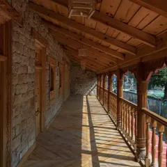 The restored upper floor corridor, where sunlight filters through intricately carved wooden railings, creating a dynamic play of light and shadow along the walkway.