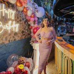 A stunning birthday setup featuring a custom "Happy Birthday" neon sign against a rustic stone wall. The scene is framed by a beautiful balloon arrangement, creating a perfect spot for birthday photos.