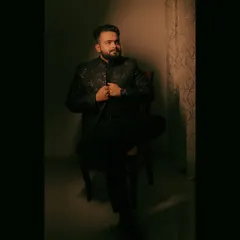 A moody, low-light portrait of the groom seated, his embroidered jacket catching the single light source.