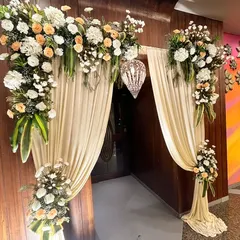 An exquisite floral entryway we designed for a special occasion. The arch is decorated with lush arrangements of white and peach roses, draped with soft fabric to create a grand and welcoming entrance.