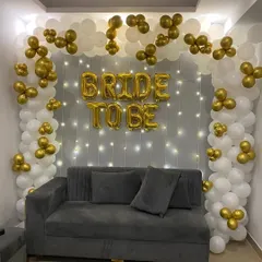 A classic and elegant 'Bride to Be' decoration for an at-home celebration. The white and gold balloon arch frames the seating area, while a curtain of fairy lights adds a warm, sparkling effect. (Also shown in images 5, 6).