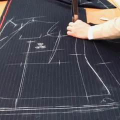 Precision in every cut. Our tailor uses traditional techniques to cut the fabric for a pinstripe suit, ensuring every pattern aligns perfectly for a seamless and professional finish.