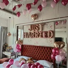A beautiful 'Just Married' bedroom decoration. The room is filled with pink, magenta, and rose gold balloons on the ceiling and bed, with large foil letters above the headboard, creating a romantic and celebratory welcome for the newlyweds.