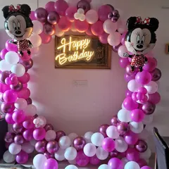 A Minnie Mouse themed birthday party decoration. I used a circular balloon arch with pink, purple, and white balloons, Minnie Mouse foil balloons, and a central 'Happy Birthday' neon sign.