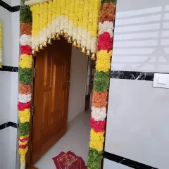 A vibrant main door decoration using thick garlands of colorful flowers. The arch is adorned with small brass bells that jingle as guests arrive.