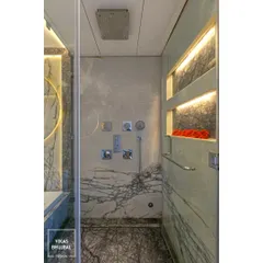 A view into the shower cubicle, featuring marble-clad walls and integrated, backlit niches for storage. The high-end chrome fixtures and rain shower head complete the luxurious experience.
