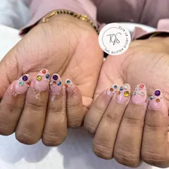A playful and colorful crystal manicure. This set features a sheer pink base with a variety of large, colorful gems placed near the cuticles for a fun and bold look.