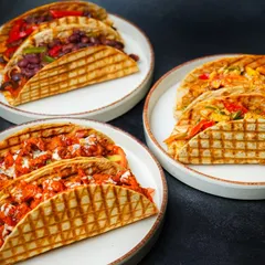 A delicious spread of assorted tacos, showcasing different fillings like paneer, chicken, and beans, served on three separate plates. This group shot captures the variety of a menu, making it a great choice for restaurant promotions.
