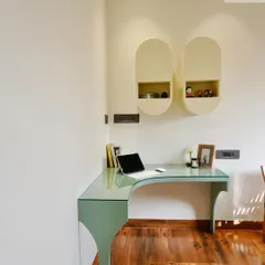 A closer look at the custom-designed study corner. The curved glass-top desk in a soft green shade is space-efficient, while the unique wall-mounted capsule shelves provide stylish storage for books and decor.