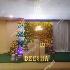 A grand party setup with a gold sequin wall, a multi-colored balloon tree, and light-up marquee letters for the name.
