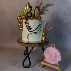 Another take on the one-line art style, this time with a black acrylic cutout. The cake is decorated with dried grasses and gold spheres for a modern, bohemian look.
