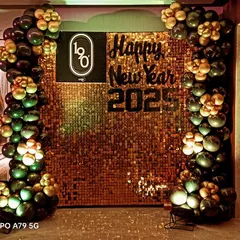 A New Year's party backdrop that also highlights the company brand. This design for '1o8' features their logo on a glittering gold sequin wall, framed by festive black and gold balloons.