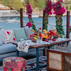 A vibrant, bohemian lounge setting by the sea in Turkey. The colourful textiles and fresh flowers create a relaxed yet celebratory atmosphere for a welcome event or mehendi.