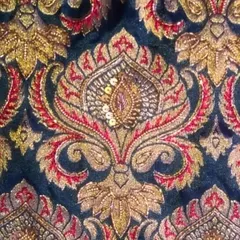 This is a detailed look at a hand-embroidered motif inspired by Banarasi weaving. The combination of gold and red thread with sequins creates a rich, three-dimensional texture on the fabric.