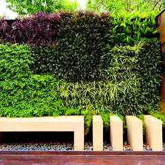 This living wall combines different species of plants to create a block-like pattern of varied textures and shades of green and purple. A simple stone bench is integrated into the design, making the wall not just a visual feature but a functional part of the garden.