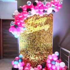 A modern and glamorous birthday photo booth with a gold shimmer sequin wall. The setup is completed with a custom neon sign and a vibrant pink and black balloon arch, perfect for chic celebrations.