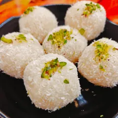 These are our Nariyal Laddoos, or coconut laddoos. Made with fresh coconut and condensed milk, they are soft, chewy, and garnished with pistachios for a delightful and light sweet treat.