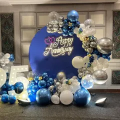 A grand 25th anniversary party with a royal blue, silver, and white theme. The decor includes a large circular backdrop, a "Happy Anniversary" neon sign, and marquee numbers celebrating the silver jubilee.