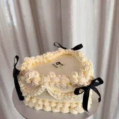 A beautiful vintage-style cake in a unique rectangular heart shape. The off-white buttercream is detailed with intricate piping and finished with small black bows for a classic look.