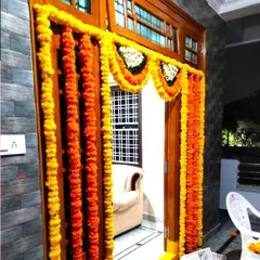 A traditional marigold flower decoration for a housewarming. The door is framed with garlands of yellow and orange marigolds and white flowers.