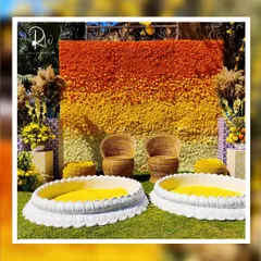 A stunning Haldi backdrop made entirely of marigolds in shades of orange and yellow, creating a beautiful ombre effect. The wicker seating and lotus-shaped basins for turmeric paste complete the traditional yet stylish look.
