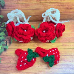 This sweet little set includes a pair of crochet baby shoes with bright red rose details and a matching pair of strawberry hair clips. Everything is made from soft yarn, perfect for a baby's comfort.