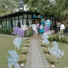 First impressions matter, and this Dior-inspired entrance sets a tone of outdoor elegance. The landscaped walkway is lined with custom cutouts of rocking horses and prams, leading guests toward a beautiful celebration under the trees.