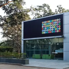 The exterior of a repurposed industrial shed in Okhla, now a modern office. The design retains the building's original character while adding a contemporary facade and large glass openings that connect the workspace to the landscape.