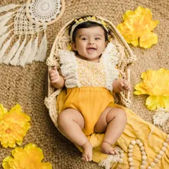 An adorable overhead shot of a baby girl during her 6-month milestone shoot. She lies in a wicker basket surrounded by yellow flowers and boho decor.
