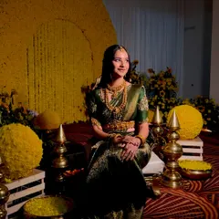 An elegant Haldi setup with a large circular backdrop made of yellow chrysanthemums. The bride is seated amidst floral spheres and traditional brass lamps.
