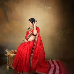 The vibrant red of this saree symbolizes love and new beginnings. This portrait, set against a painterly backdrop, captures a moment of quiet reflection and the timeless grace of an expecting mother.