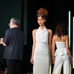 A candid moment on stage with the models. This shows the final looks, including a creative curly updo and a chic peplum top with matching pants, just before the final walk.