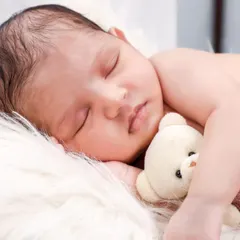 A sleeping newborn cuddles a tiny teddy bear, adding a touch of sweetness to this classic portrait on a white fur background.
