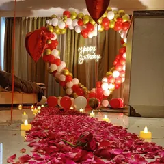 A romantic birthday surprise in a bedroom. We created a magical atmosphere with a heart-shaped balloon arch, a candle-lit path of rose petals, and "Happy Birthday" neon lights.