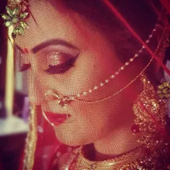 This artistic shot uses dramatic red lighting and the bride's veil to create a moody and romantic portrait. Her bold red lip and defined eyes stand out beautifully.