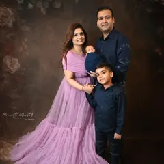 A beautiful family of four with their newborn. The mother's flowing lavender gown adds a soft touch of color to this elegant portrait against a dark, floral-painted backdrop.