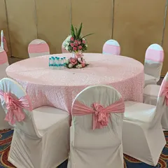 An elegant table setting for the First Holy Communion party. The tables are dressed in pink textured linens with matching chair sashes, and a simple floral centerpiece completes the look.