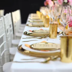 A long dining table set with gleaming gold-plated cutlery and glasses against crisp white linens. This modern and luxurious setup is perfect for an elegant wedding reception or corporate gala.