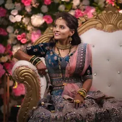 A regal reception look. The bride is seated on a throne-like chair, wearing a heavily embroidered velvet lehenga, with makeup that is both sophisticated and glamorous.