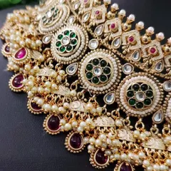 This close-up highlights the rich texture of a layered kundan necklace with green and maroon accents.