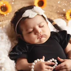 A sleeping newborn girl looking angelic in our sunflower-themed setup, holding a string of pearls.