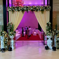 An elegant entrance featuring soft cream drapes and classic white urns filled with vintage-style florals. The design creates a warm and sophisticated welcome for a wedding at the Taj Santacruz.