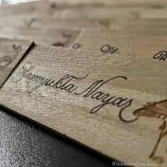 A close-up of a wooden name plate, showing the texture of the wood grain beneath the smooth calligraphy. Working on natural materials like this adds a warm, organic feel to event decor.