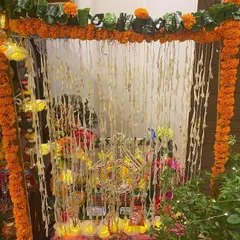 A small mandap created for a home pooja. The frame is wrapped in marigold garlands, and strings of rajnigandha (tuberose) hang in the background for a traditional look and fragrance.