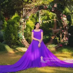 A full view of our solid purple trail gown, spread out in a garden setting. The off-shoulder neckline and the sheer volume of the fabric create a regal, princess-like effect.