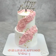 A two-tiered cake with a beautiful cascading floral design. The pink piped roses flow diagonally across the cake, accented with gold leaf for a touch of elegance.