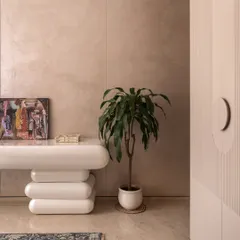 A close-up of a playfully sculptural console table. Paired with a simple potted plant, it adds character and a touch of modern art to this serene guest room corner.