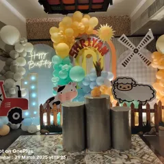 We brought the countryside to the city with this farm-themed first birthday. The setup includes a tractor cutout, a windmill prop, cute farm animal characters, and a "1" marquee number against a backdrop of soft-colored balloons.