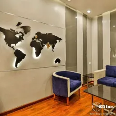 A modern office waiting area featuring a backlit world map as a statement piece. The combination of plush blue armchairs and sleek side tables creates a globally-inspired, professional ambiance.